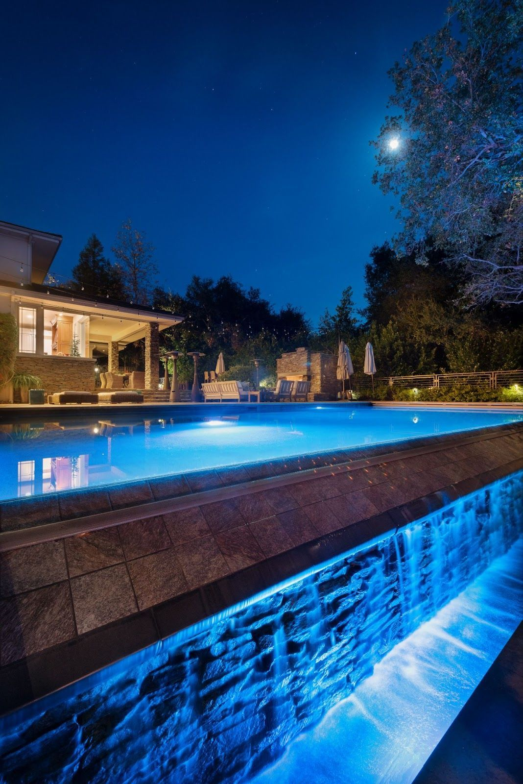 Fluidity pool design with waterfall edge and night lighting